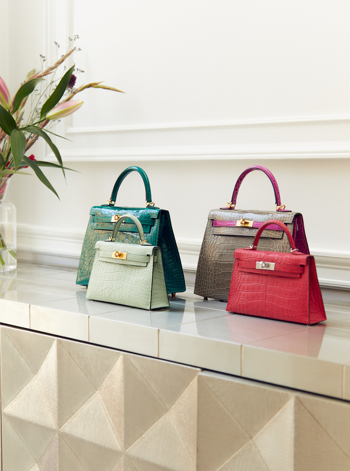Four crocodile Hermès Kelly bags arranged on a console