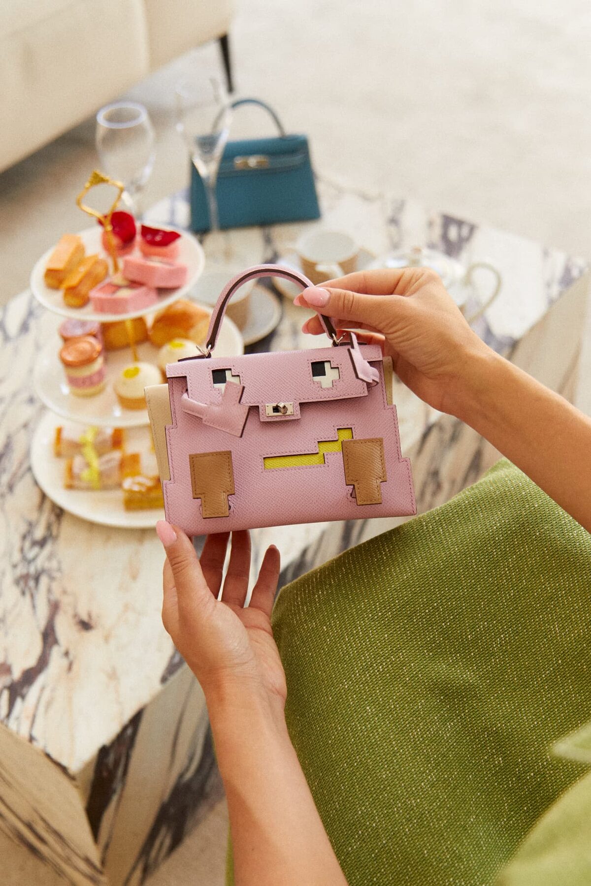 A stylised pink Hermès Kelly held beside a tray of pastries